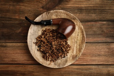 Photo of Board with smoking pipe and dry tobacco on wooden table, top view