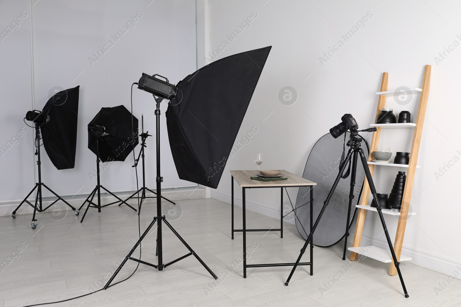 Photo of Table with stylish dinnerware in front of camera and professional lighting equipment indoors. Photo studio set