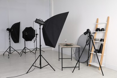 Table with stylish dinnerware in front of camera and professional lighting equipment indoors. Photo studio set