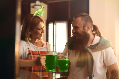 Photo of Young woman and man toasting with green beer in pub. St. Patrick's Day celebration