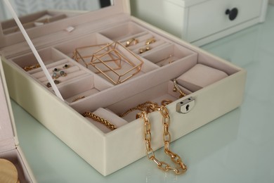 Photo of Jewelry box with stylish golden bijouterie on white dressing table, closeup