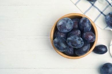 Delicious ripe plums on white wooden table, flat lay. Space for text