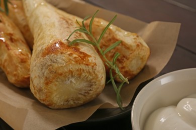 Photo of Tasty baked parsnips with rosemary and sauce on wooden table, closeup
