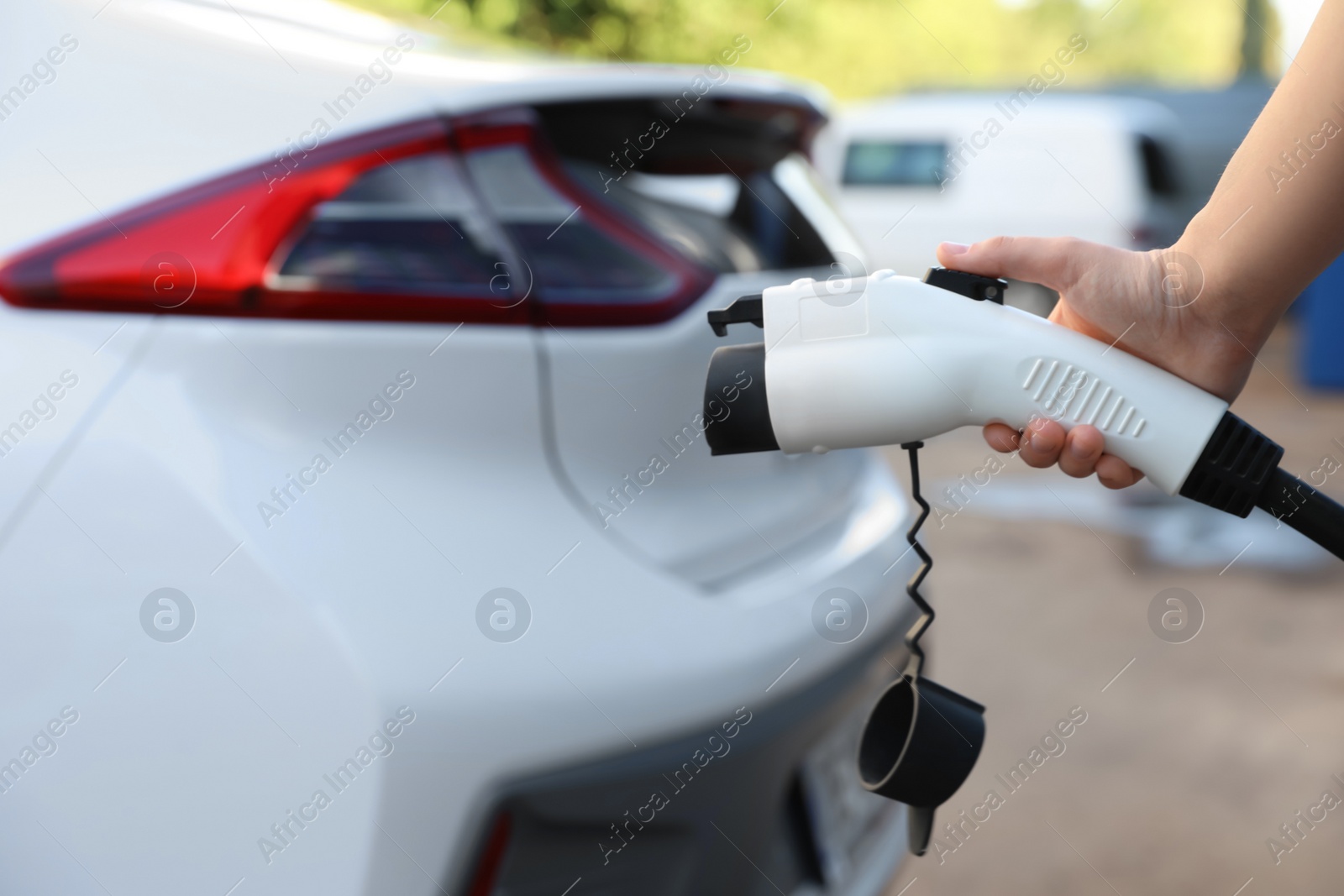 Photo of Woman holding power supply cable at electric vehicle charging station, closeup