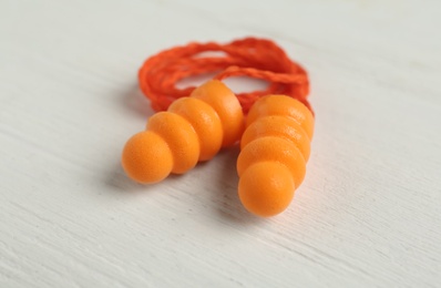 Photo of Pair of orange ear plugs with cord on white wooden background, closeup