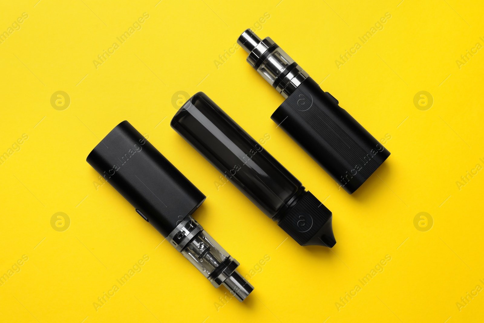 Photo of Electronic cigarettes and vaping liquid on yellow background, flat lay