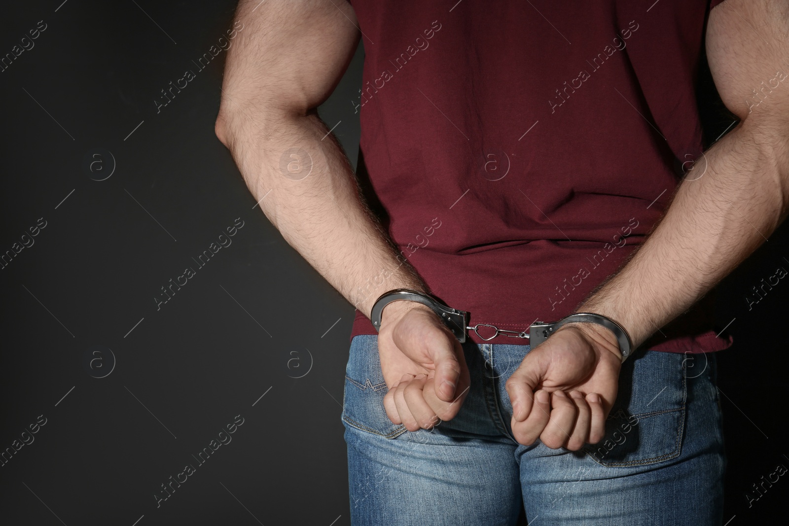 Photo of Male criminal in handcuffs near black wall, closeup