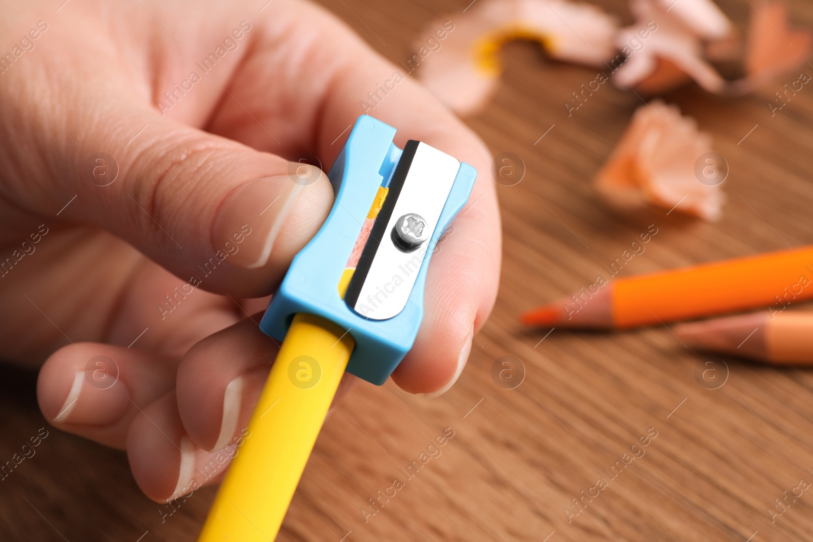 Photo of Woman sharpening yellow pencil at wooden table, closeup