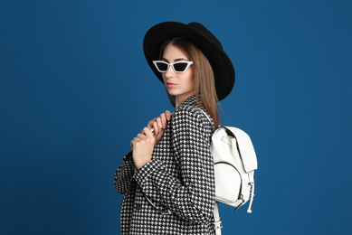 Beautiful young woman in sunglasses with stylish bag on blue background