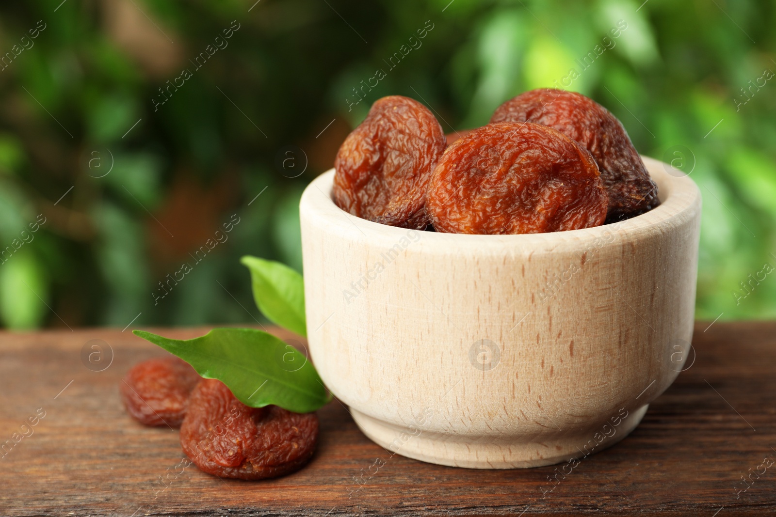 Photo of Bowl of tasty apricots on wooden table against blurred green background, space for text. Dried fruits