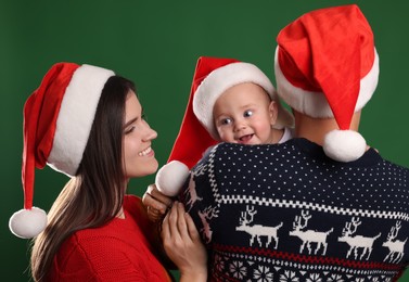 Photo of Happy couple with cute baby in Christmas outfits and Santa hats on green background