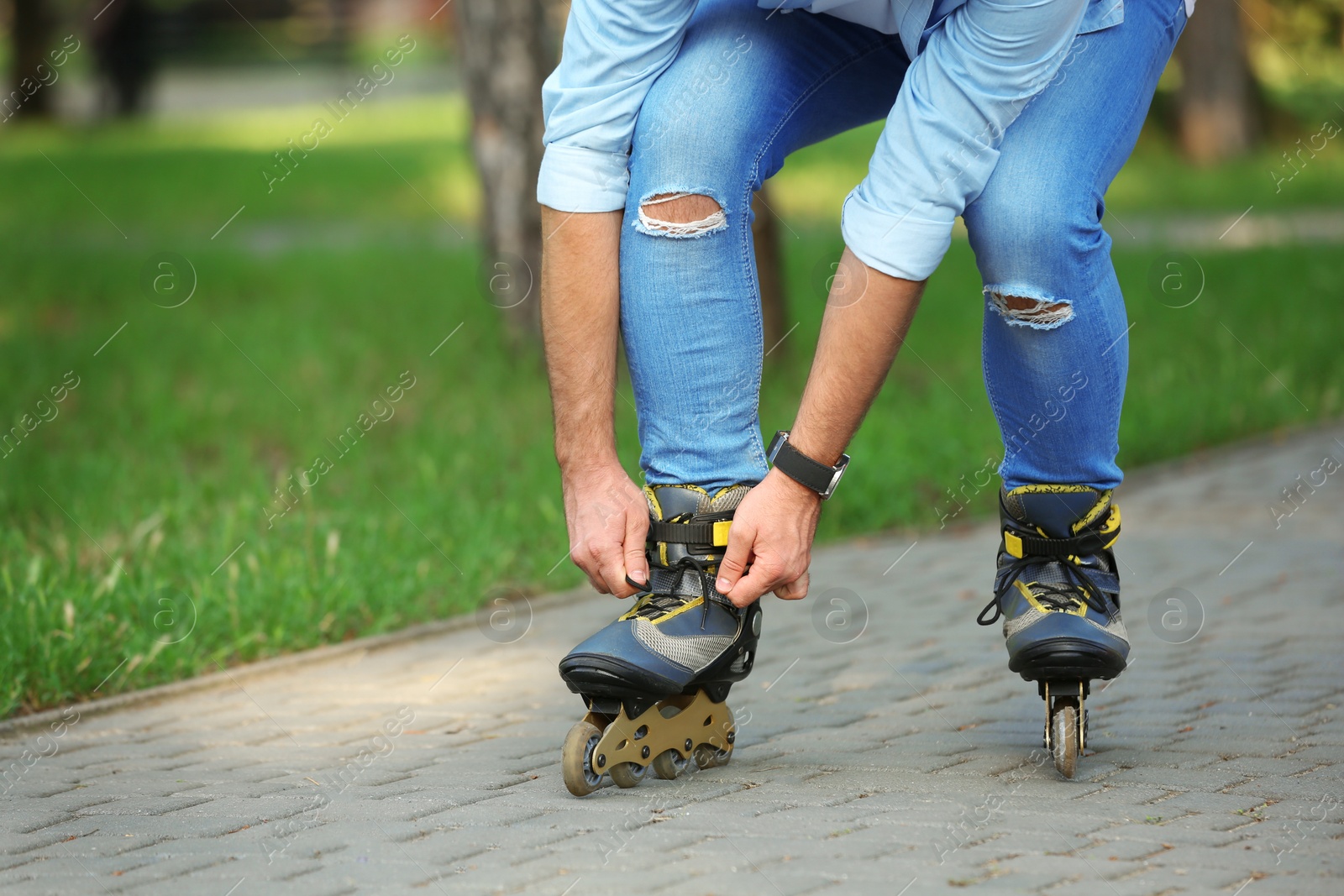 Photo of Man fixing roller skates in summer park, closeup