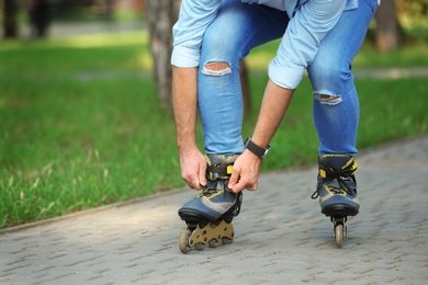 Man fixing roller skates in summer park, closeup