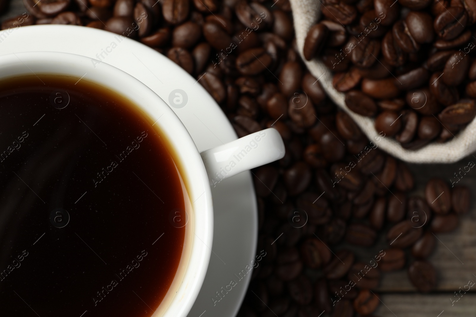 Photo of Cup of aromatic coffee and beans on wooden table, flat lay. Space for text