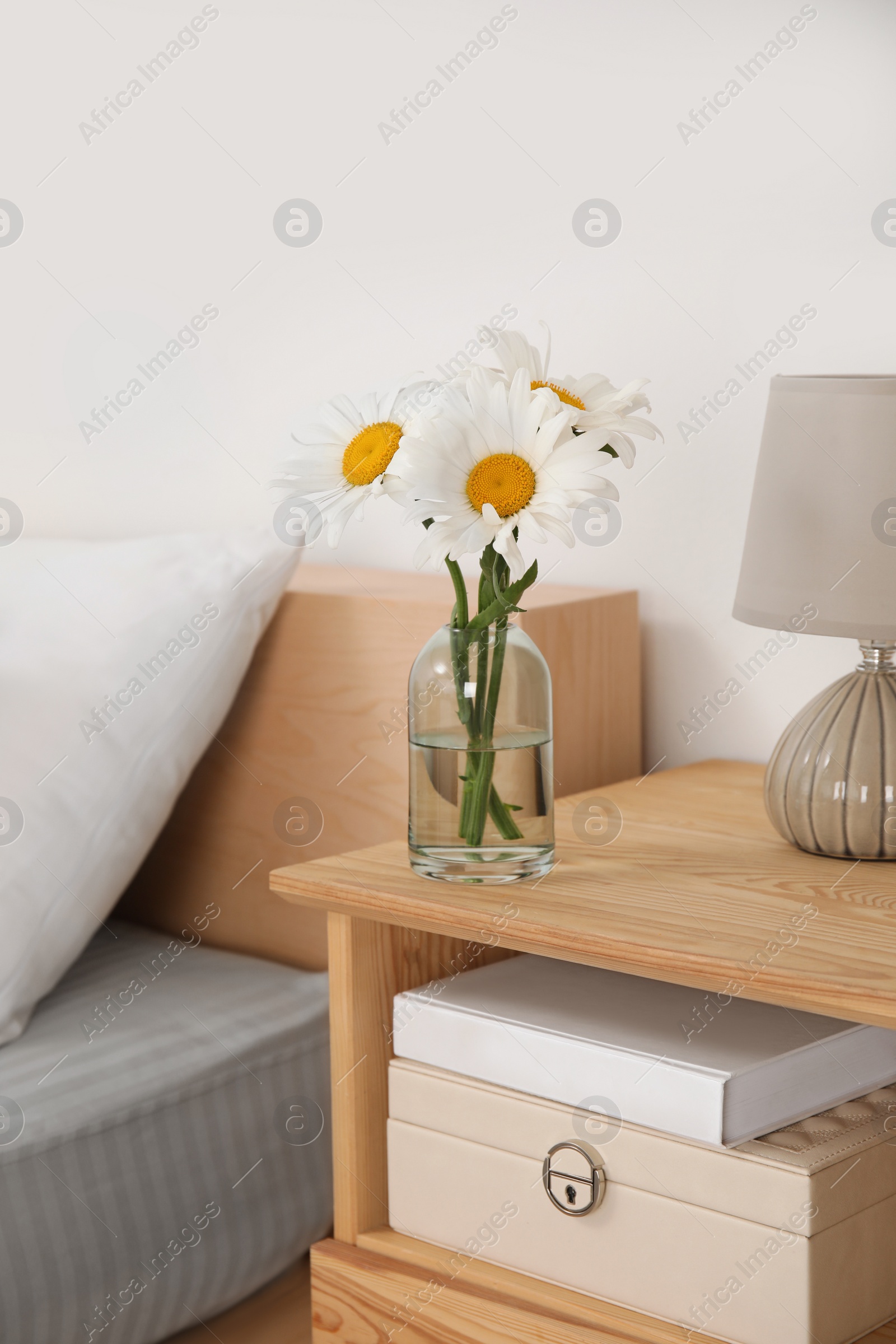 Photo of Bouquet of beautiful daisy flowers and lamp on nightstand in bedroom