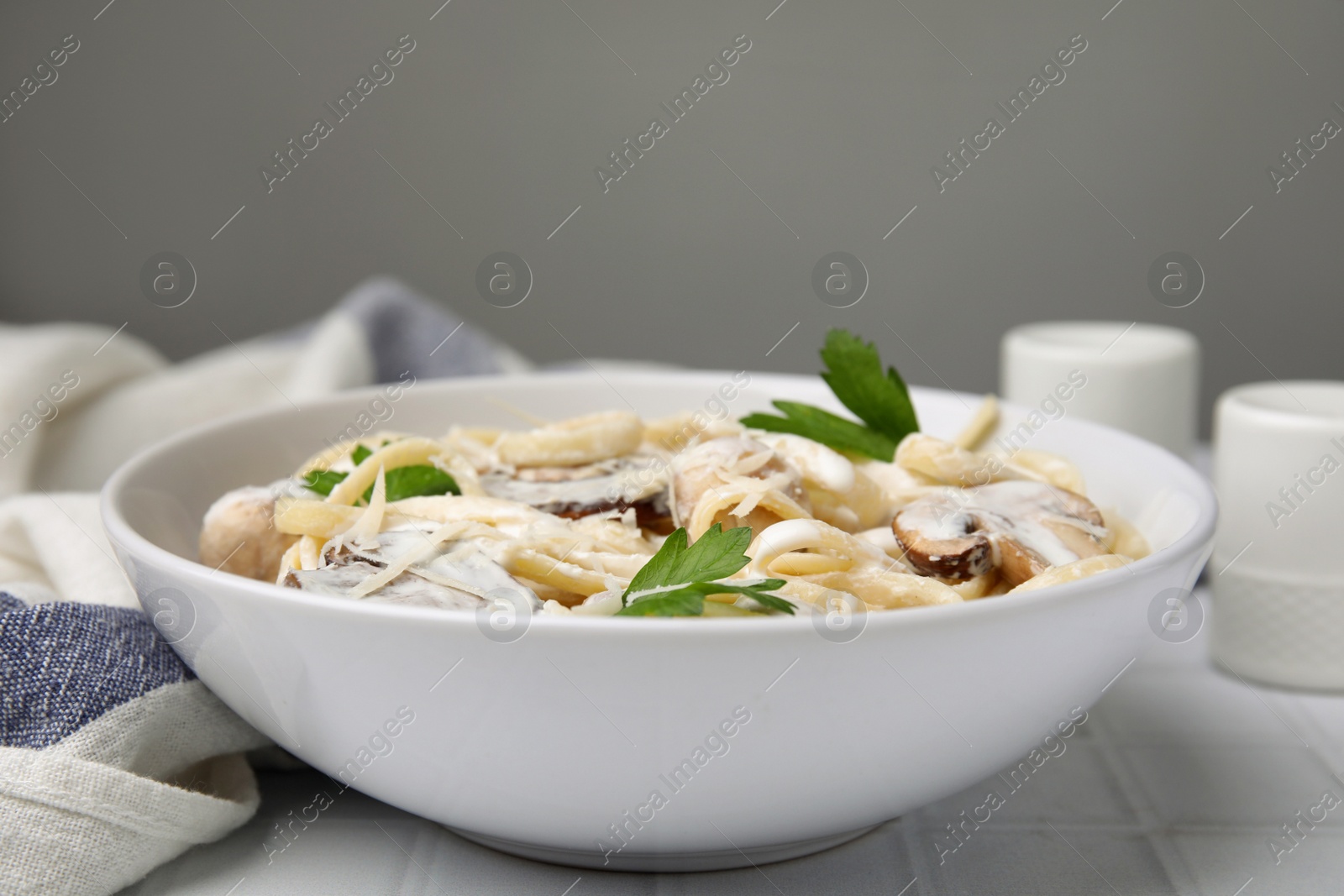 Photo of Delicious pasta with mushrooms on white tiled table, closeup