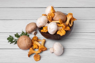 Photo of Bowl with different mushrooms and parsley on white wooden table