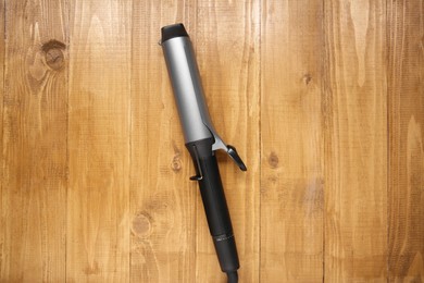 Hair curling iron on wooden background, top view
