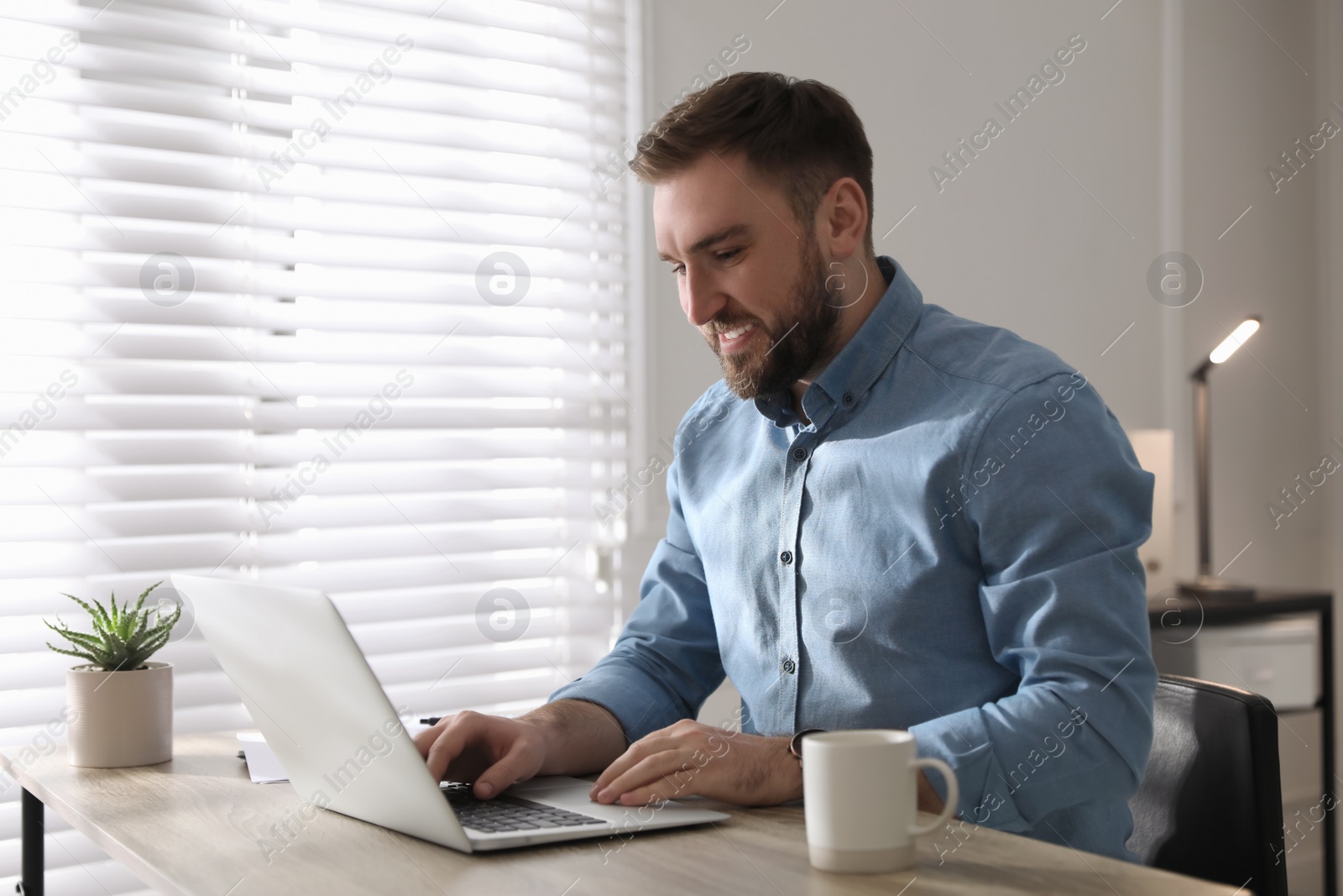 Photo of Young man working on laptop at table in office