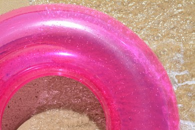 Bright inflatable ring on sandy beach near sea, top view
