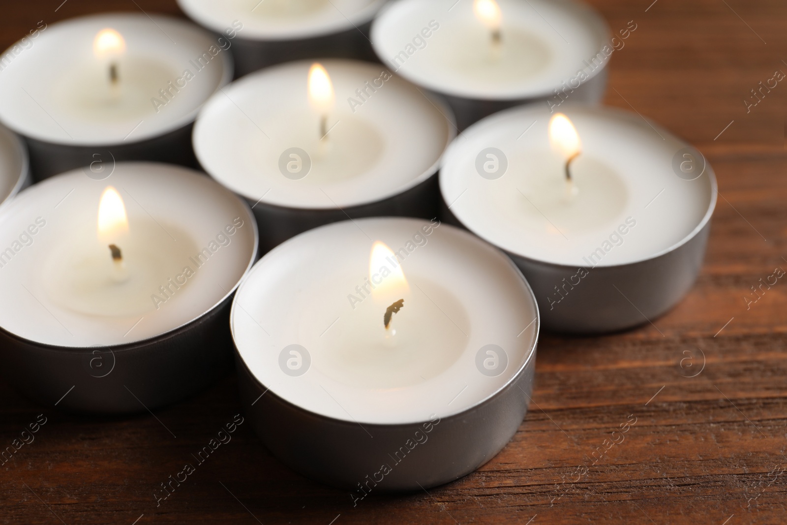 Photo of Small wax candles burning on wooden table, closeup
