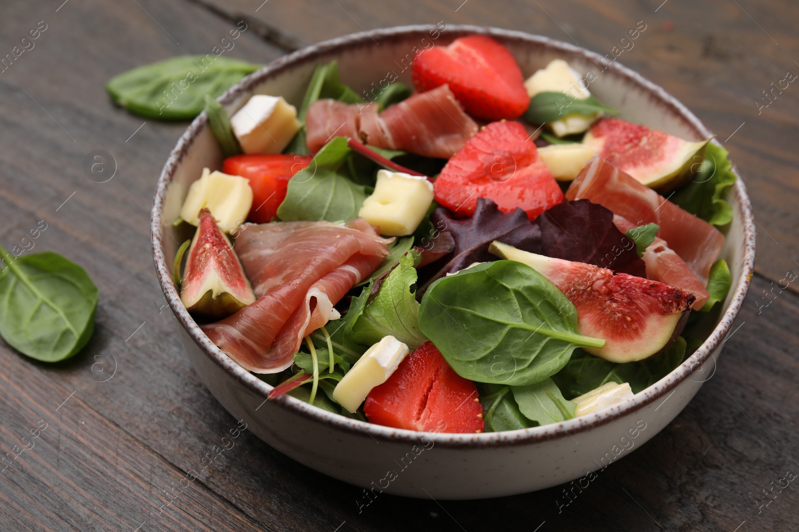 Photo of Tasty salad with brie cheese, prosciutto, strawberries and figs on wooden table, closeup