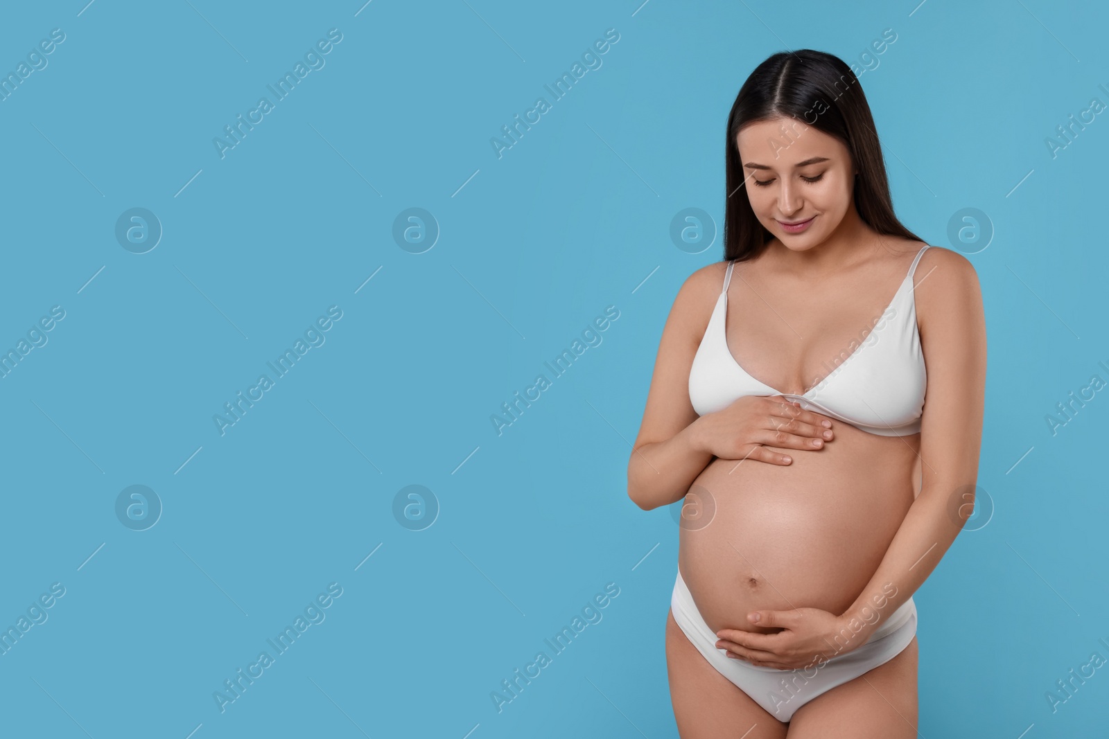 Photo of Beautiful pregnant woman in stylish comfortable underwear on light blue background, space for text