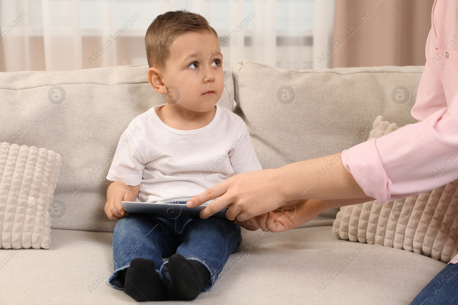 Photo of Internet addiction. Mother taking away tablet from her little son on sofa at home, closeup