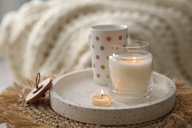 Photo of Cup of drink and burning candles on wicker mat indoors. Interior elements