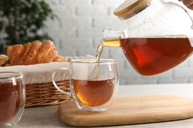 Photo of Pouring aromatic tea into glass cup at light grey table, closeup