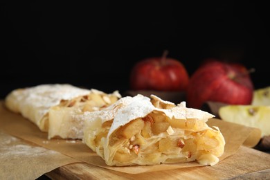 Photo of Delicious apple strudel with almonds and powdered sugar on wooden board, closeup. Space for text