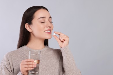 Photo of Happy woman with glass of water taking pill on gray background, space for text