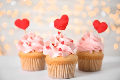 Photo of Tasty cupcakes for Valentine's Day on white table against blurred lights