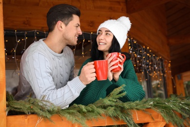 Photo of Happy couple in sweaters with cups near decorated railing