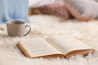 Photo of Open hardcover book on fuzzy rug indoors. Space for text