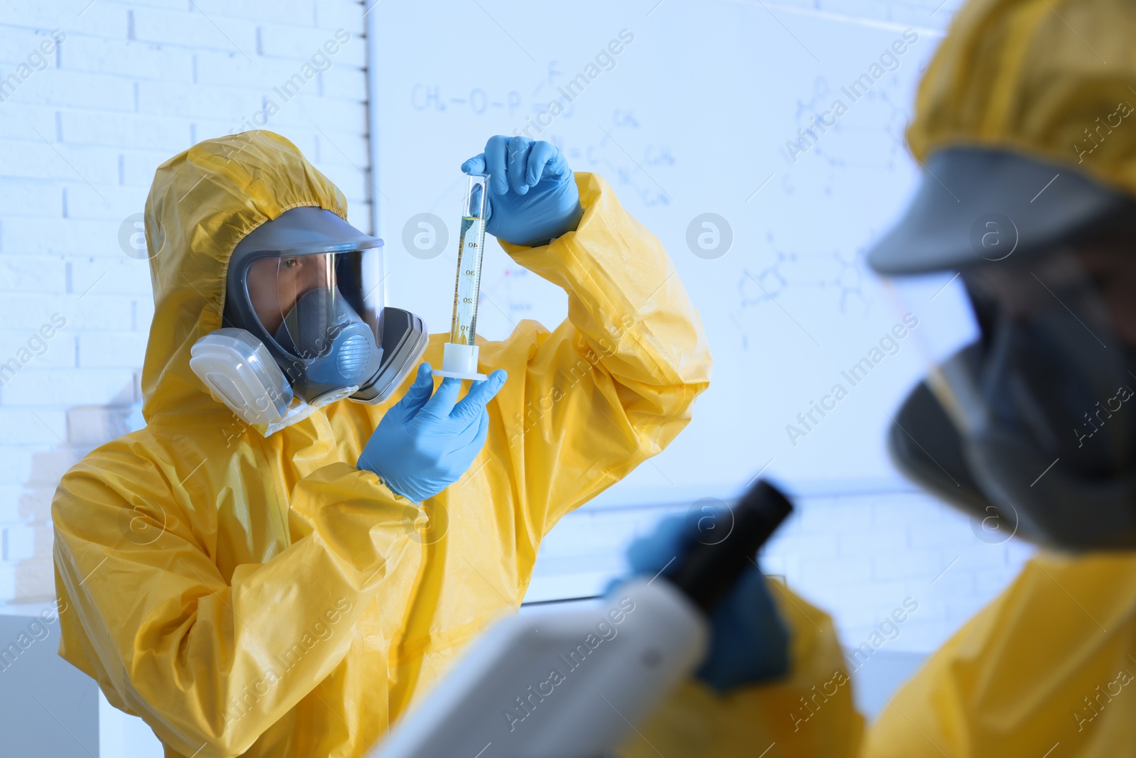 Photo of Scientist in chemical protective suit with graduated cylinder at laboratory. Virus research