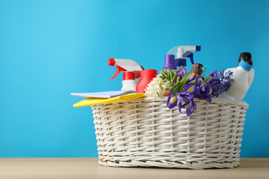 Photo of Wicker basket with spring flowers and cleaning supplies on wooden table