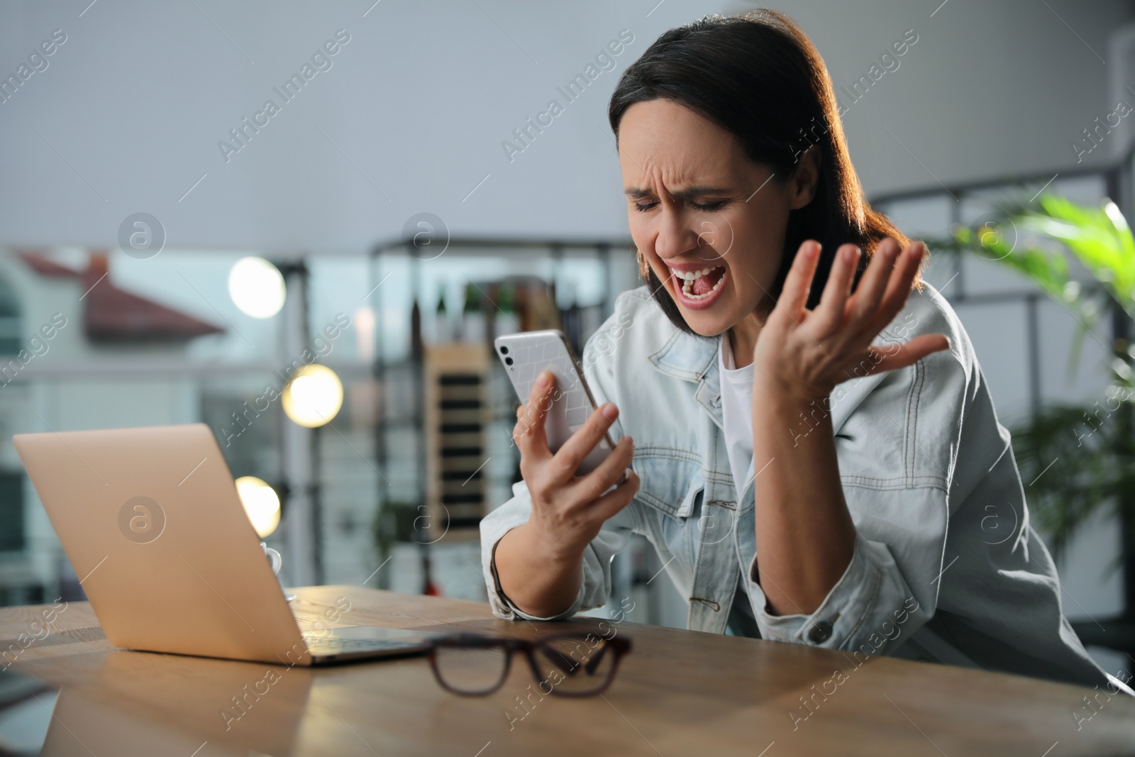 Photo of Emotional woman with smartphone at table in office. Online hate concept