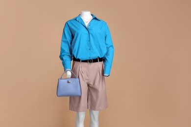 Photo of Female mannequin dressed in leather shorts and stylish light blue shirt with accessories on beige background
