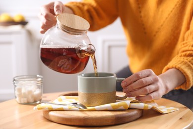 Photo of Woman pouring hot tea into cup at wooden table, closeup