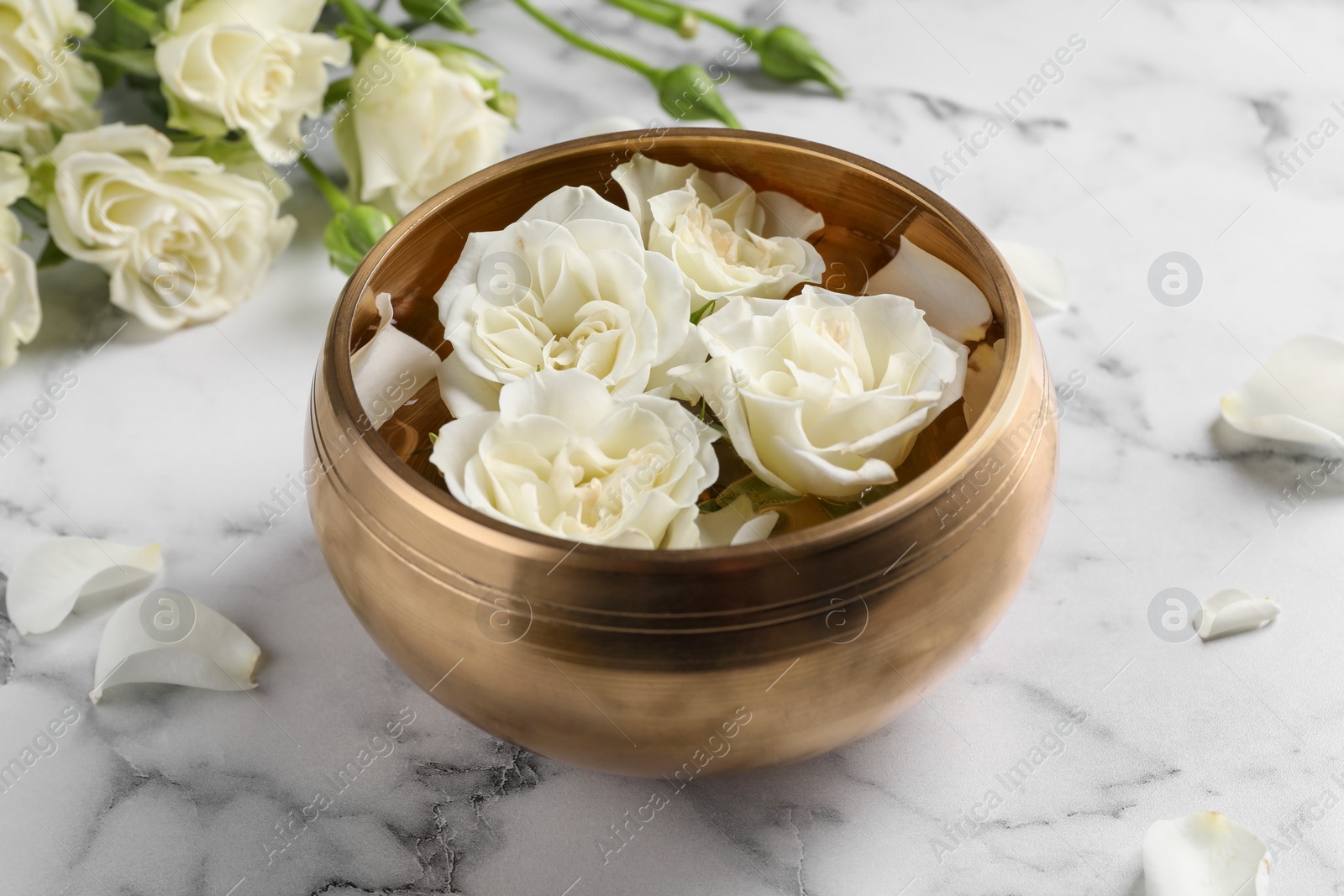 Photo of Tibetan singing bowl with water and beautiful roses on white marble table, closeup