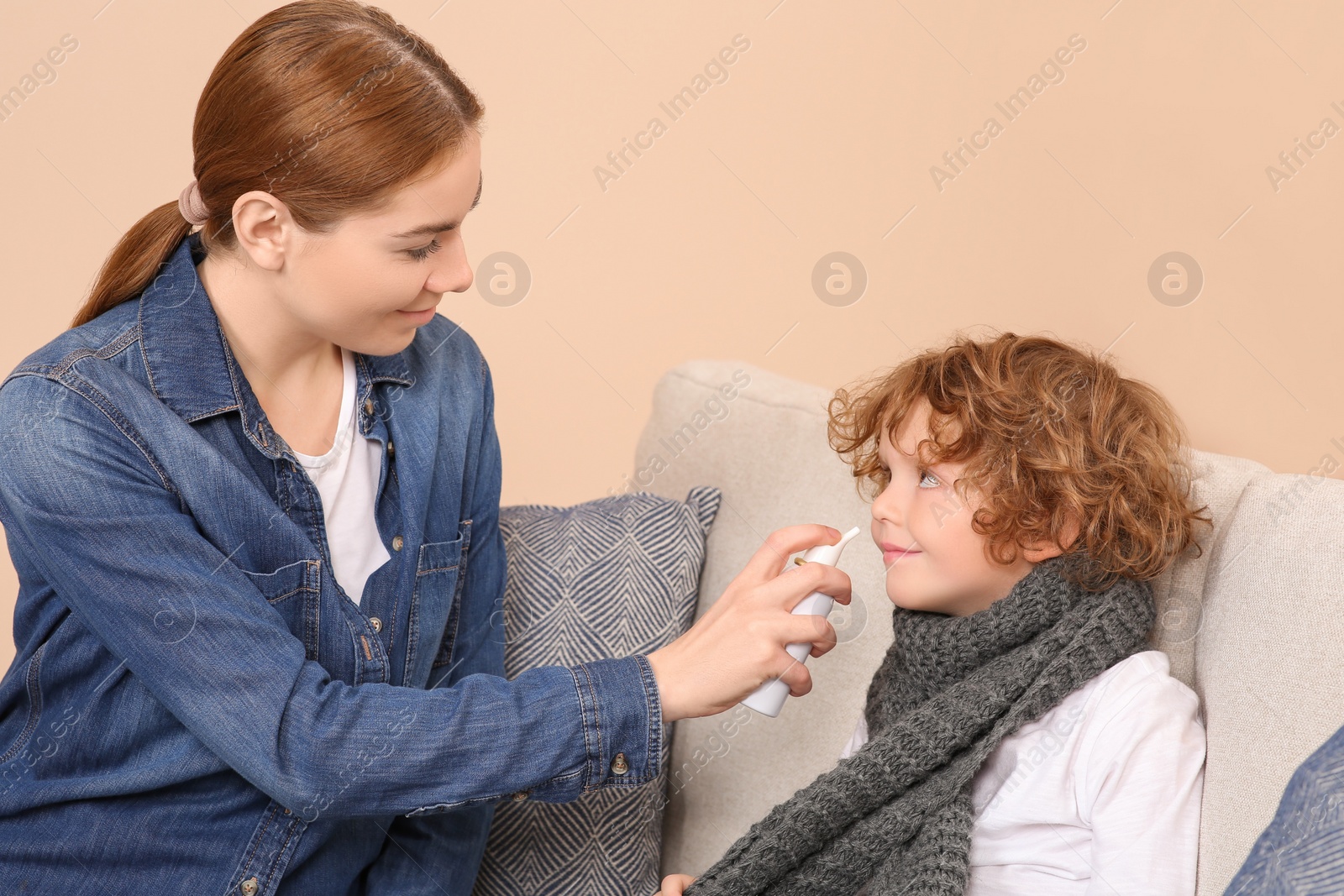 Photo of Mother using nasal spray to treat her little son on sofa indoors