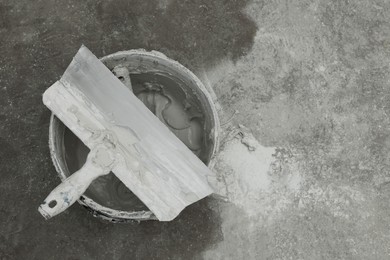 Photo of Bucket with plaster and putty knife on concrete floor, top view. Space for text