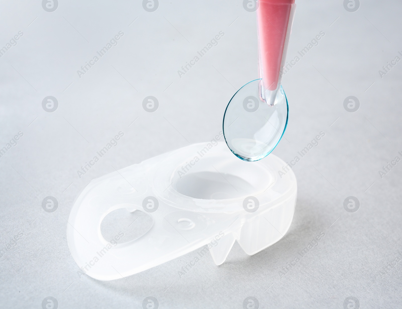 Photo of Tweezers with contact lens on light background