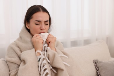 Sick woman wrapped in blanket with tissue on sofa at home, space for text. Cold symptoms