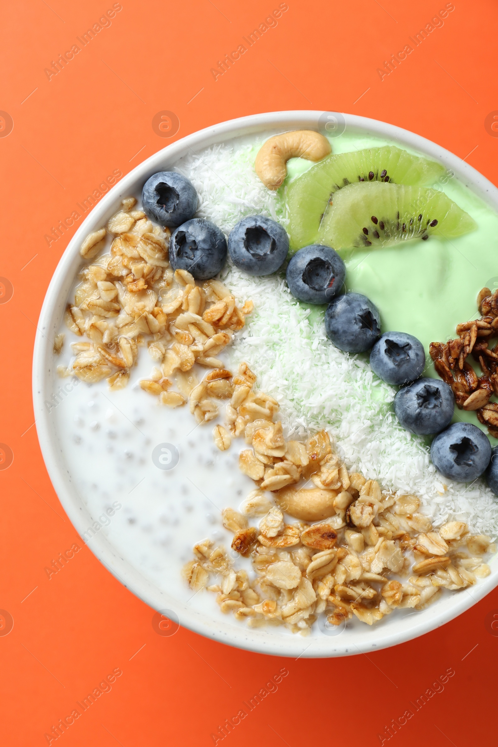 Photo of Tasty smoothie bowl with fresh kiwi fruit, blueberries and oatmeal on orange background, top view