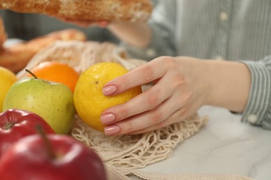 Photo of Woman taking lemon out from string bag at light table, closeup