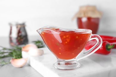 Photo of Gravy boat with hot chili sauce on table