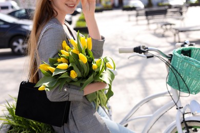 Teenage girl with bicycle and bouquet of yellow tulips on city street, closeup