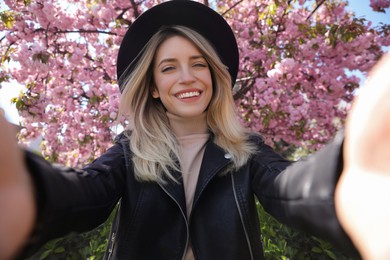 Happy woman taking selfie near blossoming sakura outdoors on spring day